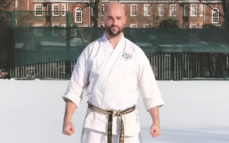 A Karate coach in white stands in snow
