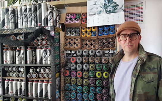 Graffiti artist and cafe owner Psych stands next to wall of spray cans