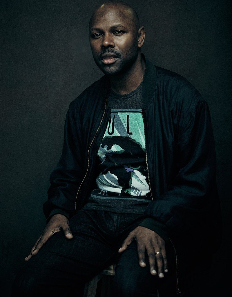 A professional image of Mr Gee. He's looking sharp down the camera. He's sitting down in front of a black back drop.