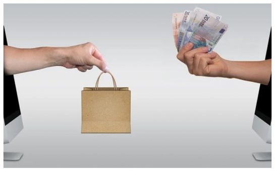 A stock image of a hand passing a small brown square paper bag to a hand holding a wad of notes.