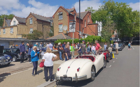Residents standing around classic cars at the car show in the sunshine.