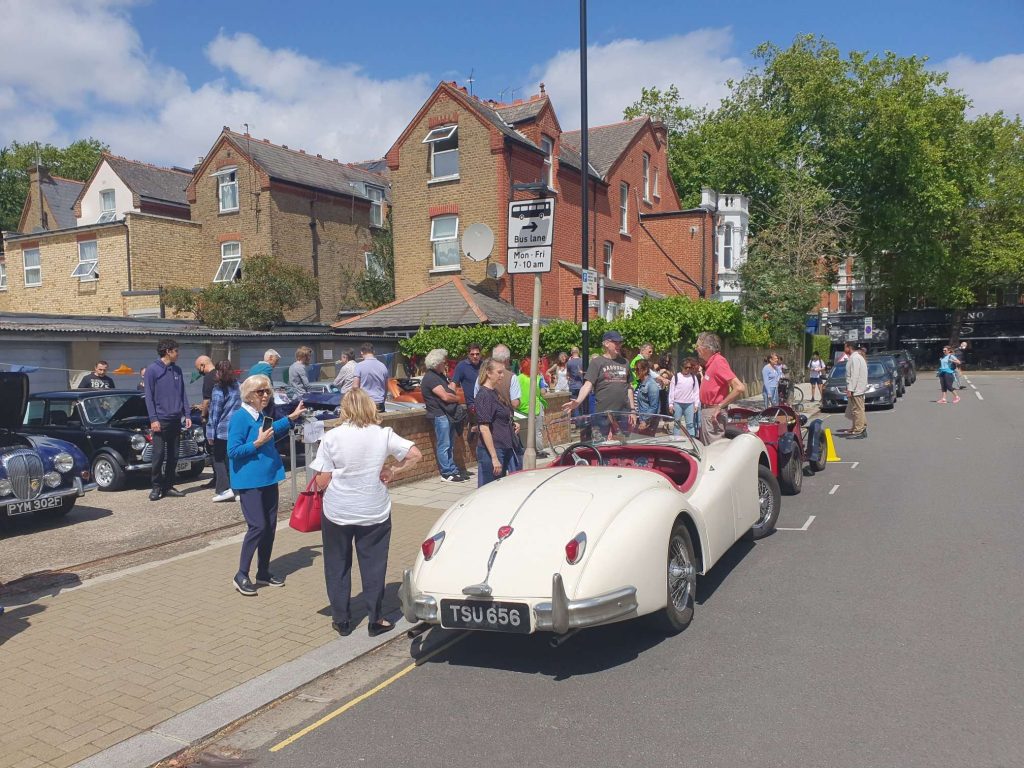 Residents standing around classic cars in the sunshine.