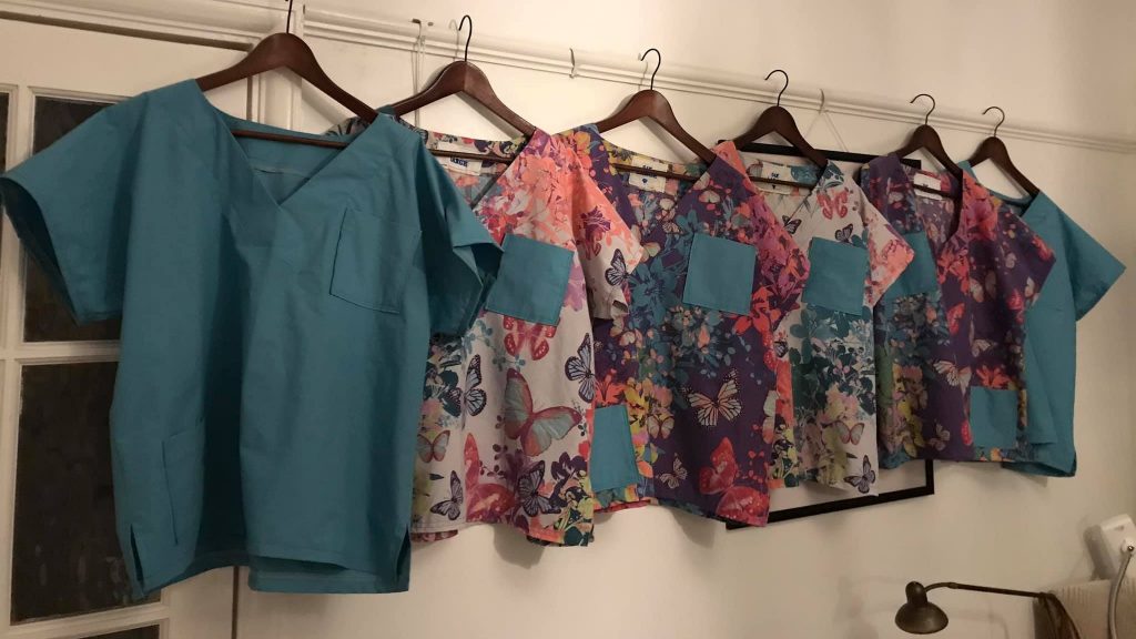 Hand-made hospital scrubs, all with different patterns, hanging up in a line.