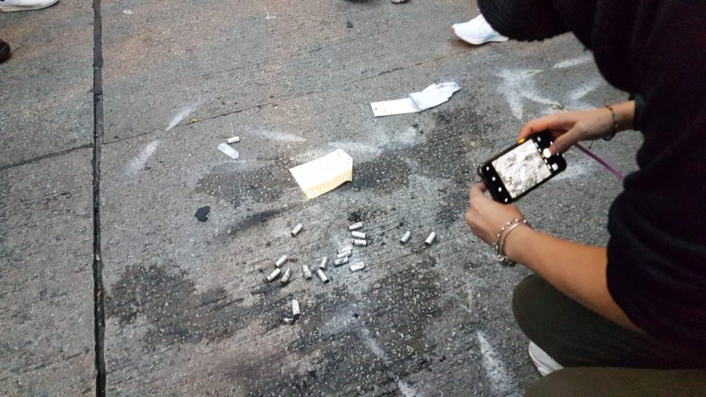 A photo of someone taking a photo on there phone of what look like bullets on the floor.