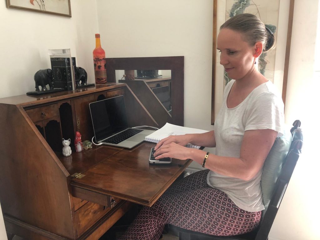 Kate Pounds sitting at her desk typing on the braille device. 