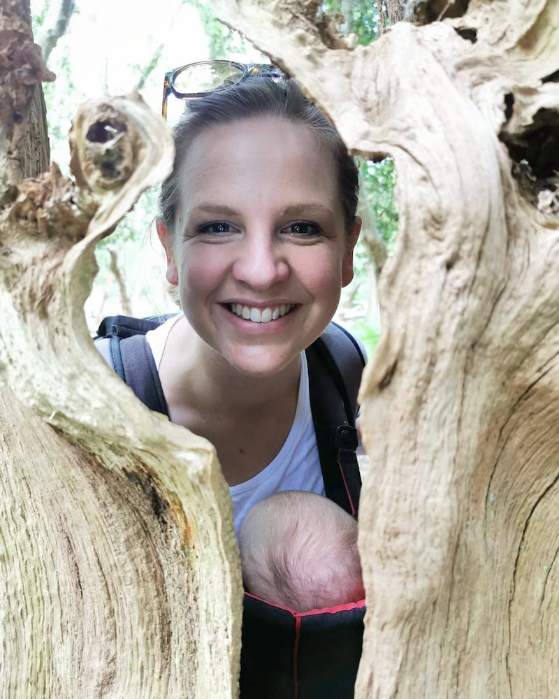 Megan Lock smiles through a gap in a tree with her baby on her front
