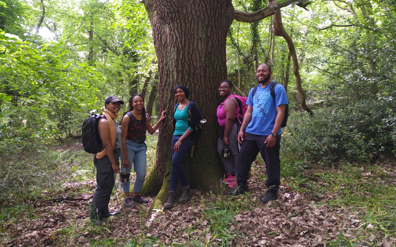 Wild in the City participants relax beneath a tree. They're wearing colourful clothes and have big grins on their faces