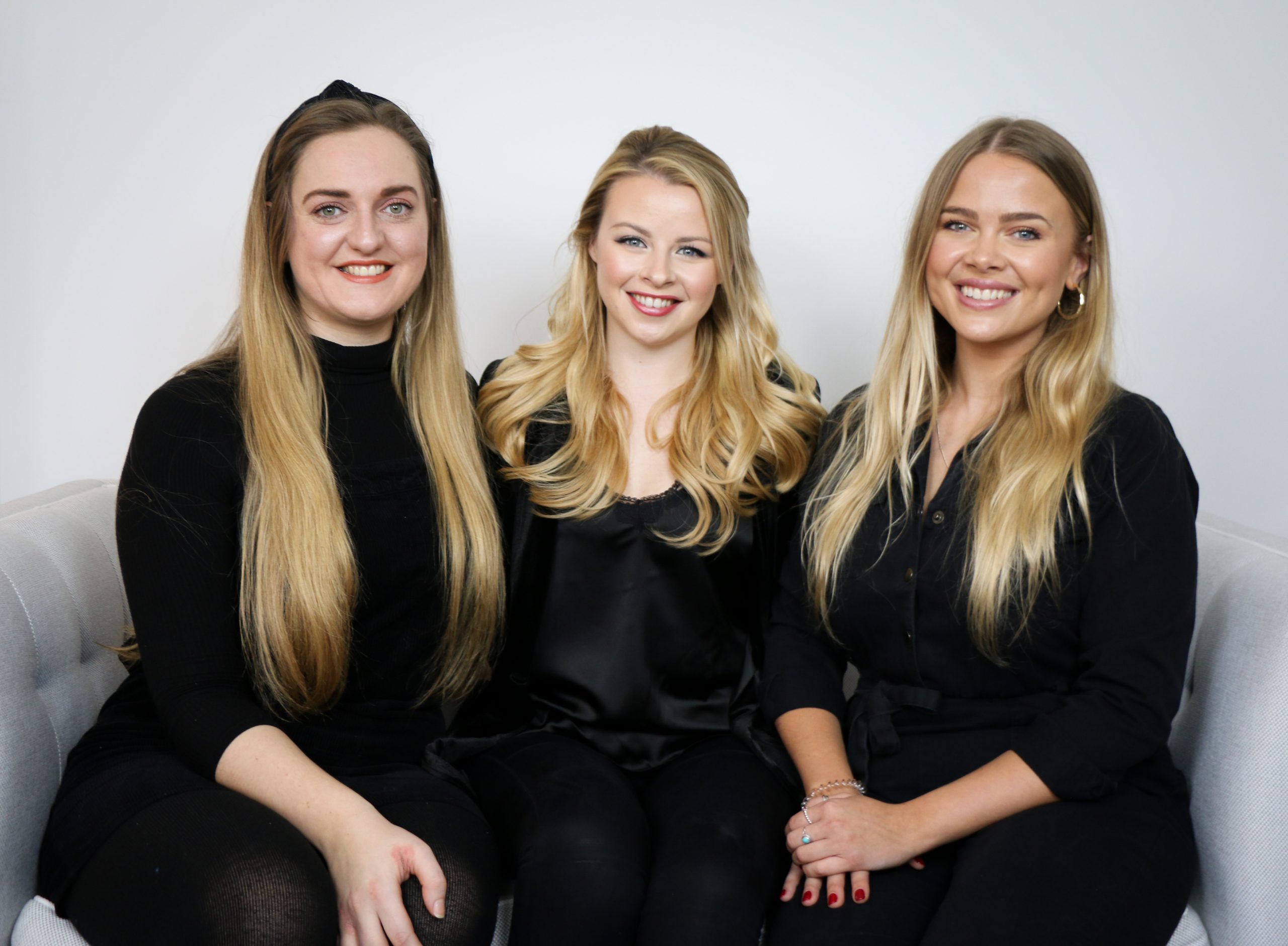 Three women in black clothing with long blonde hair sitting next to each other and smiling at the camera. They are the owners of Richmond performing arts school WestWay.