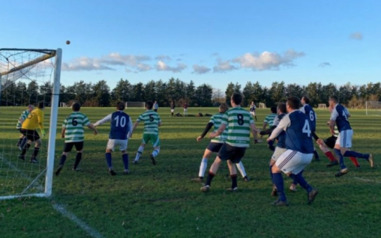 Footballers playing near a goal in a grassroots football game as a corner comes in