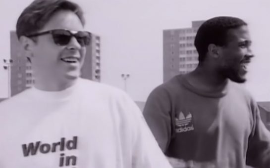 Bernard Sumner singing next to John Barnes during the 'World In Motion' music video