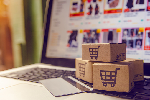 A stock image of a laptop with three little brown cardboard boxes with shopping trollies on the keyboard next to a credit card.