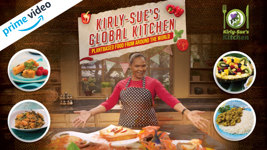 A promotional image for Kirly-Sue's Global Kitchen. She wears an apron and spreads her arms wide, smiling. Dishes that will appear on the show are superimposed over the photo e.g. a salad and a chickpea curry.