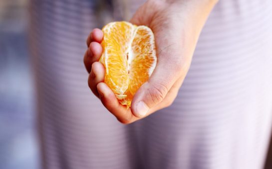 Women's reproductive health. A dressed woman holding half an orange in front of her pelvic area.