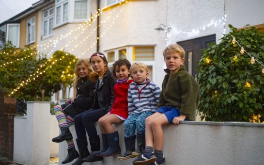 Children sitting on wall in front of fairy lights