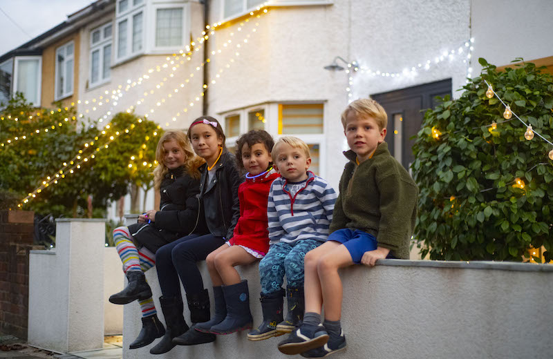 Children sitting on wall in front of fairy lights