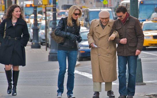 Two people helping an elderly man down the street