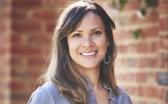 Nohelia Rambal in a blue shirt, smiling in front of a red brick wall