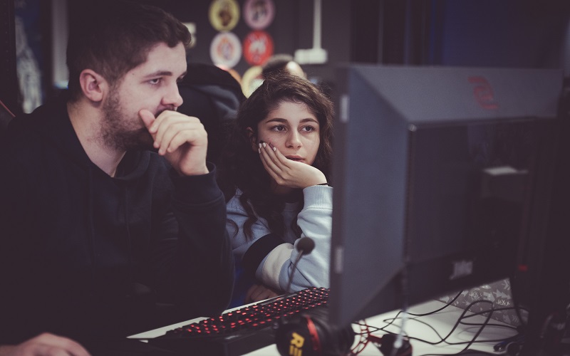 A man and Lily Jahan sit in front of a computer monitor in the esports arena looking at it intently 