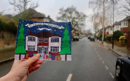 a picture of a house is held up by a hand at the entrance to a street