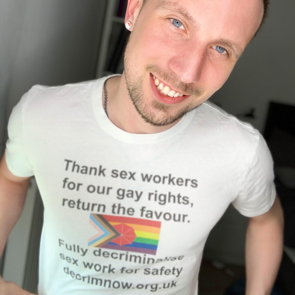 Jason Domino smiles. He wears a t-shirt: "Thank sex workers for our gay rights, return the favour"