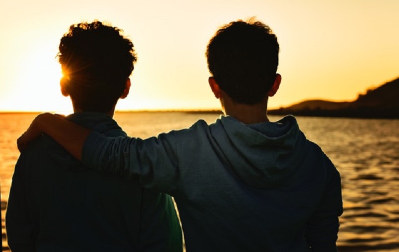 two boys sat by the sea as the sun sets