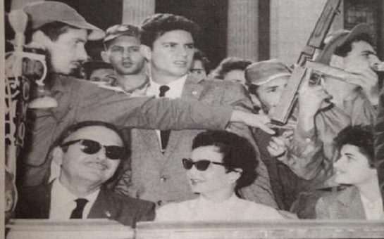 Picture of Helen's great aunt Ellie in Cuba, wearing sunglasses, in a crowd of people with a man holding a gun