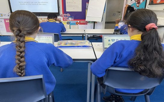 Two school pupils in blue and yellow uniform learning on laptops.