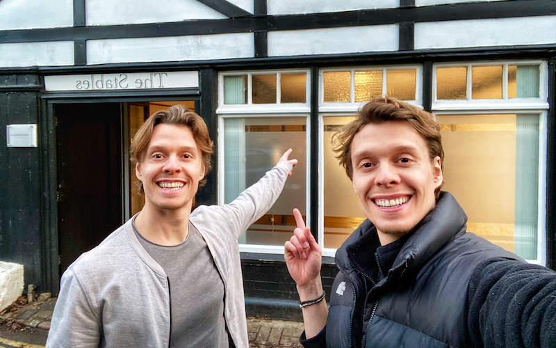 twins stand in front of new studio space, smiling