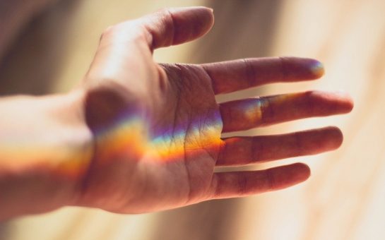 A hand with a rainbow light shining over it.