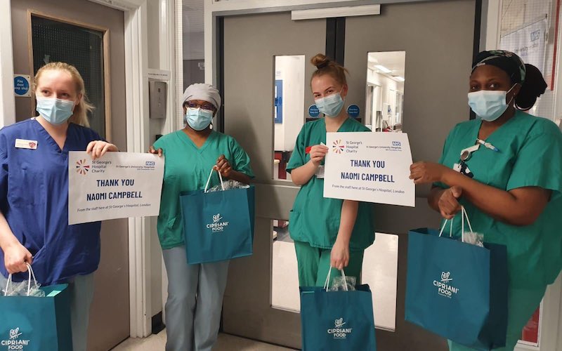 four members of NHS staff in scrubs hold gift bags and signs reading thank you naomi campbell