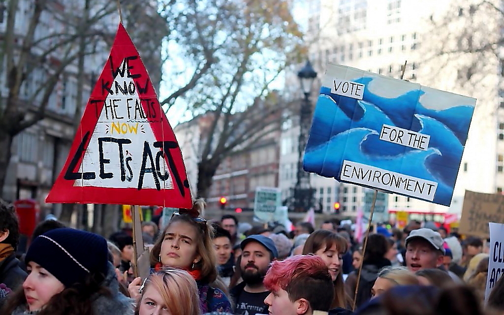 A mass of young people. A long haired person holds up a triangular sign with a red border: "We know the facts, now let's act." Another placard is in the air: "Vote for the environment."