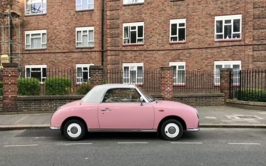 A pink car parked on a road outside a block of flats.