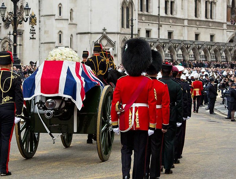 Queens guard accompanying a horse drawn carriage carrying a coffin draped in the Union Jack.
