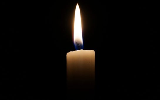A small white lit candle with a yellow frame on a black background. The image illustrates a story about online books of condolences.