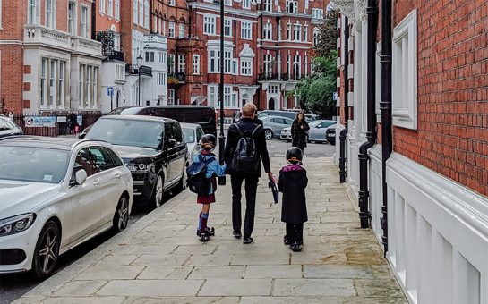 An adult and two children walk along Kensington street on a cloudy day
