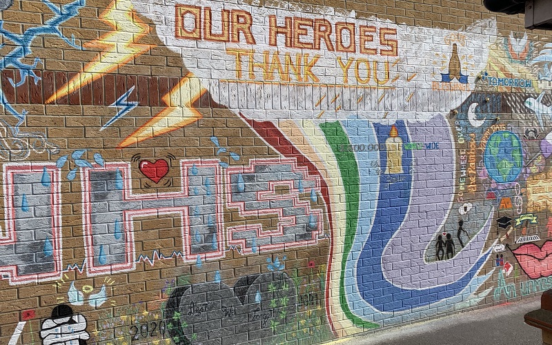 The NHS mural with detail of tributes to the over 100,000 people killed by COVID-19 in the UK and a stone heart with the words "Lest We Forget" inscribed onto it.