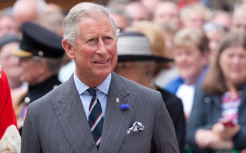 Prince Charles walking. A crow of people stand behind him