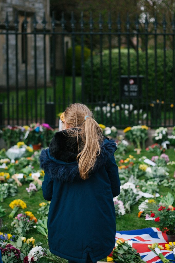 The back of a young girl in a blue coat looking at the flowers on the ground.