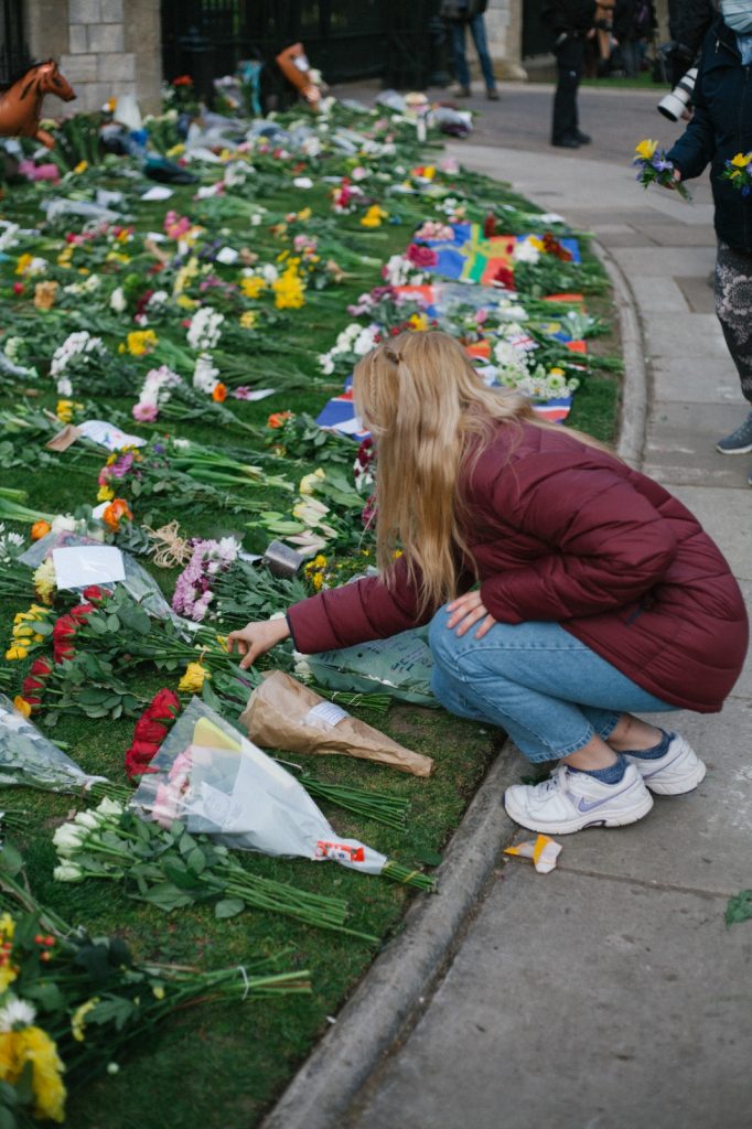 A young girl in a red coat laying flowers on the grass. 