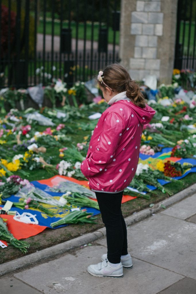 The back of a young girl in a pink coat looking at the flowers on the ground.