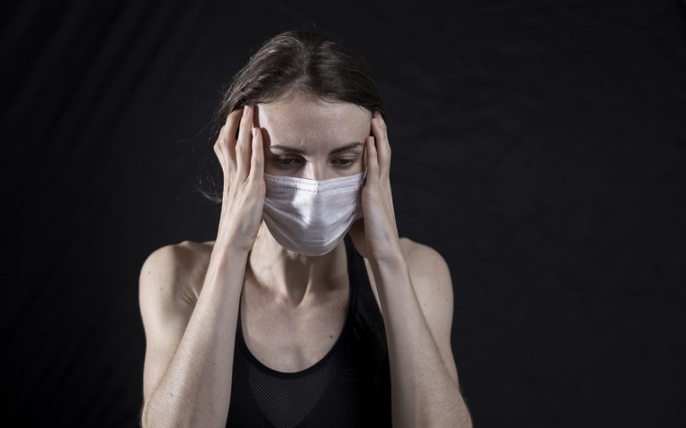 woman wearing mask with head in hands