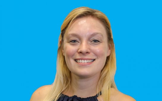 portrait of hannah ginnett on blue background. she is blonde and smiling