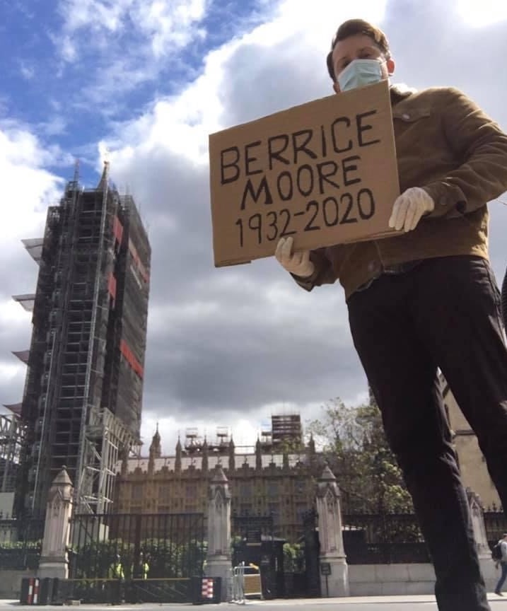 Ellis Tustin holds a cardboard headstone dedicated to his late grandfather Berrice Moore whilst standing outside the Houses of Parliament