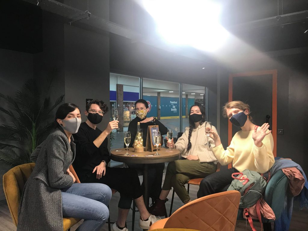 A group of five people toast successfully escaping the Alice in Puzzleland escape room with prosecco at high bar stools. 