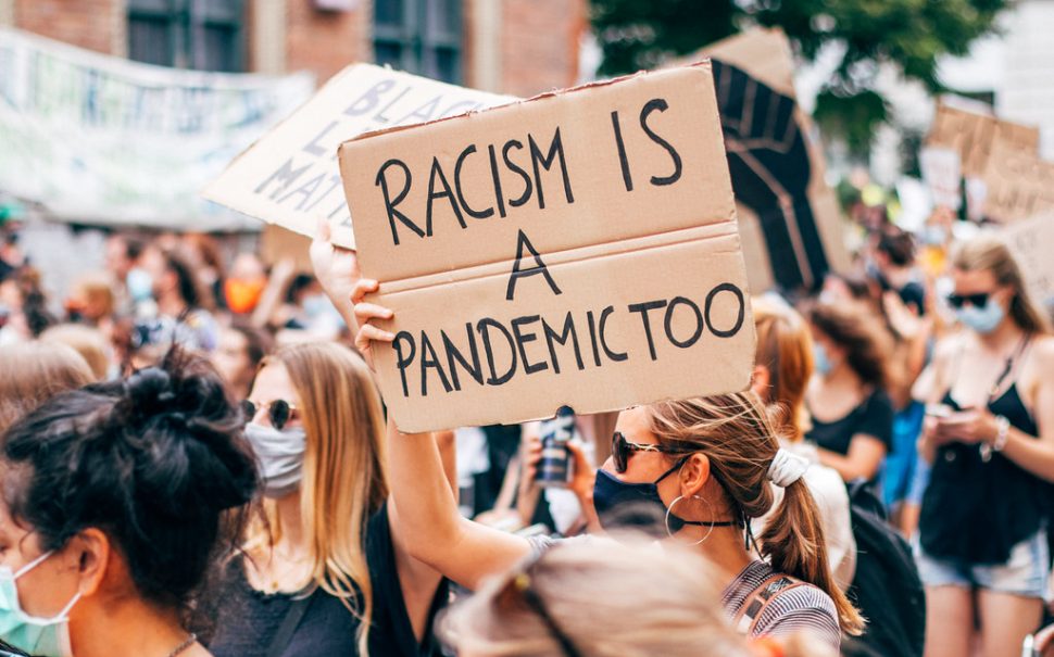 Black Lives Matter female activist holding a sign with a message Racism is a Pandemic Too