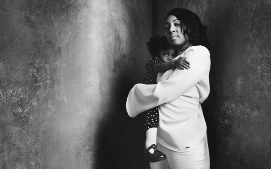 Woman holds her child in a dark room with bare walls