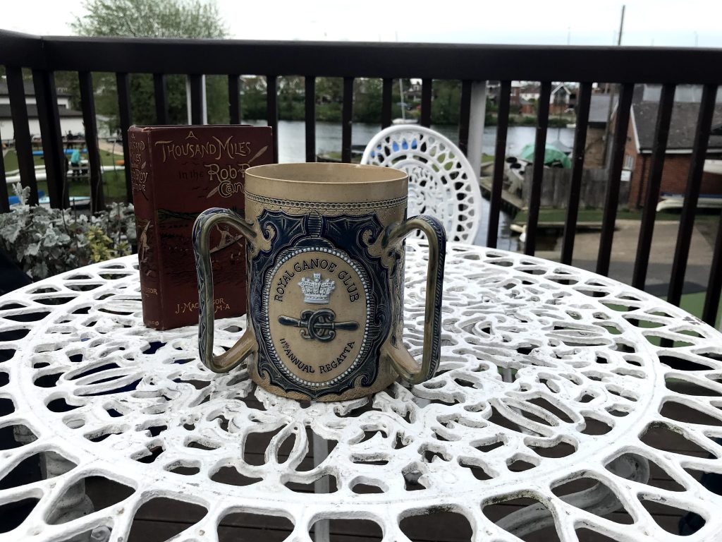 Ceremonial ceramic cup with the Royal Canoe Club logo embossed on it for its annual regatta. Showing the history of the club. Also a first edition copy of A Thousand Miles by John MacGregor who was an explorer who founded the club. 