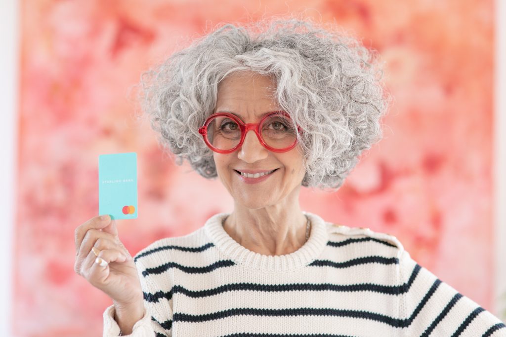 Elderly woman with red frame glasses holding Starling Bank debit card