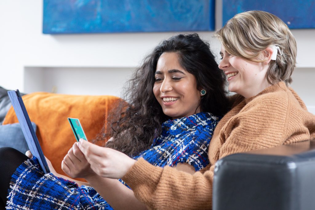 Same-sex couple with iPad and debit card. One partner wears a hearing aid.