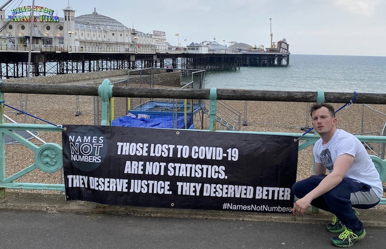Ellis Tustin crouches with his banner in front of Brighton pier.